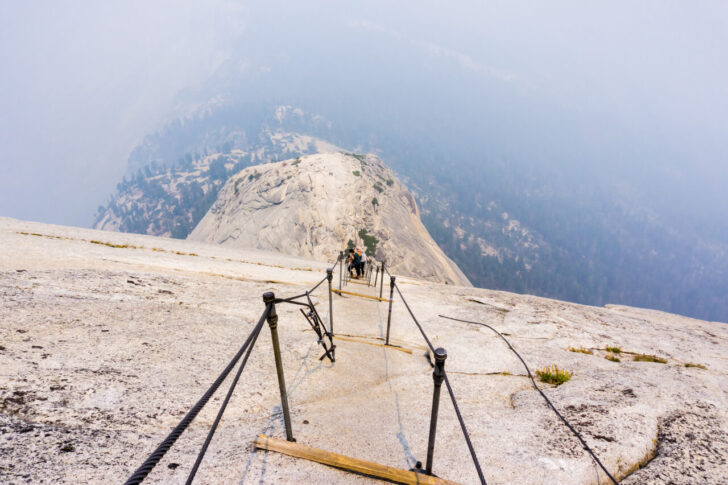 Looking down on the Half Dome cables on a summer day; smoke covering the sub dome and the valley beyond; Yosemite National Park