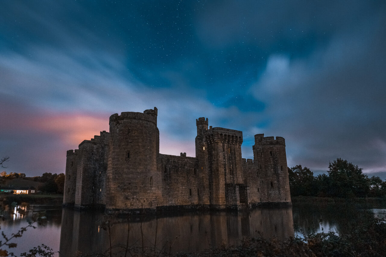 Bodiam Castle in a lake under a starry sky with long exposure in the evening in the UK